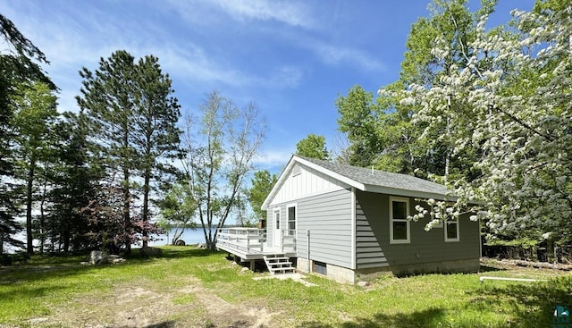 view of home's exterior featuring roof with shingles, a deck, board and batten siding, and a yard