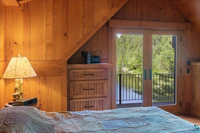 bedroom featuring french doors, a water view, wood walls, and access to outside