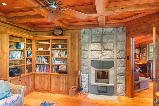 living area with beamed ceiling, a fireplace, light hardwood / wood-style floors, wood walls, and wooden ceiling