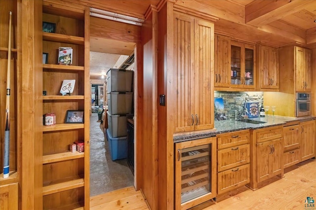 kitchen with dark stone countertops, wine cooler, oven, light hardwood / wood-style flooring, and beamed ceiling