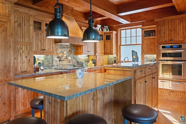 kitchen with gas cooktop, stainless steel double oven, a breakfast bar area, decorative light fixtures, and a kitchen island