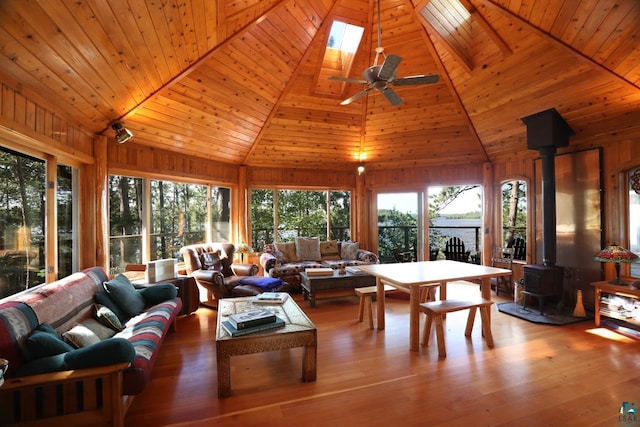 sunroom featuring vaulted ceiling with skylight, a ceiling fan, wooden ceiling, a wood stove, and a water view