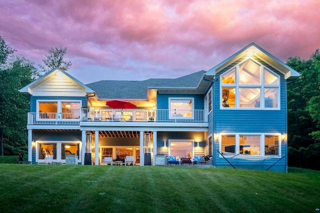 back house at dusk featuring a balcony and a yard