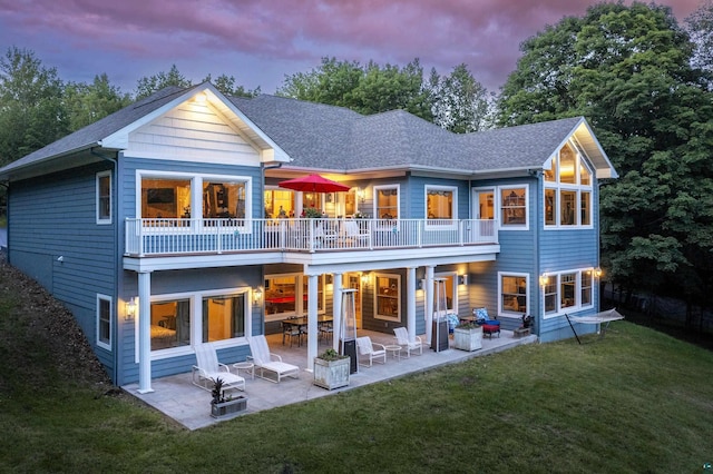 back of property at dusk featuring a patio, a yard, and a shingled roof