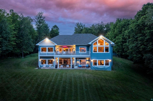 back house at dusk featuring a patio, a balcony, and a yard