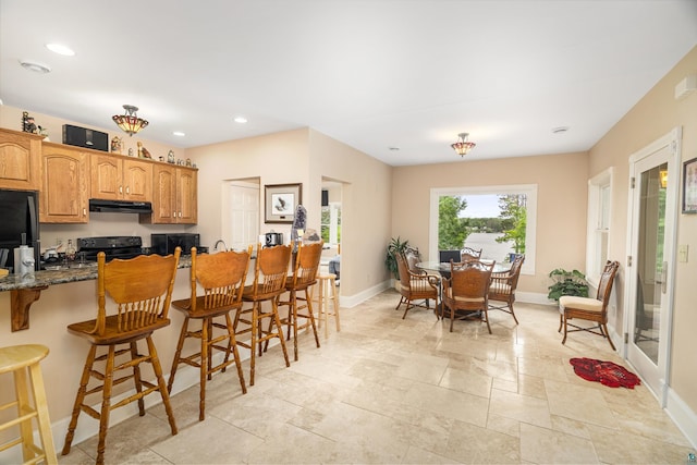 kitchen featuring black appliances, a breakfast bar, dark stone countertops, and exhaust hood