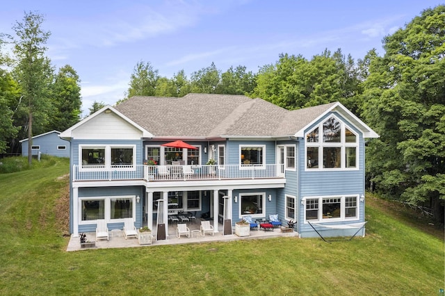 rear view of house with a shingled roof, a patio, and a lawn