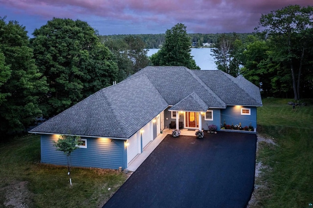 ranch-style house with driveway, a water view, a wooded view, and roof with shingles