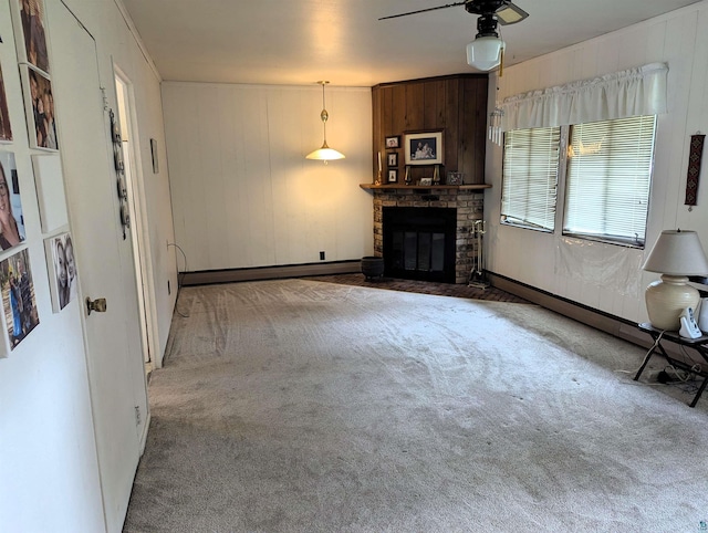 unfurnished living room with ceiling fan, a baseboard heating unit, carpet flooring, a brick fireplace, and wood walls