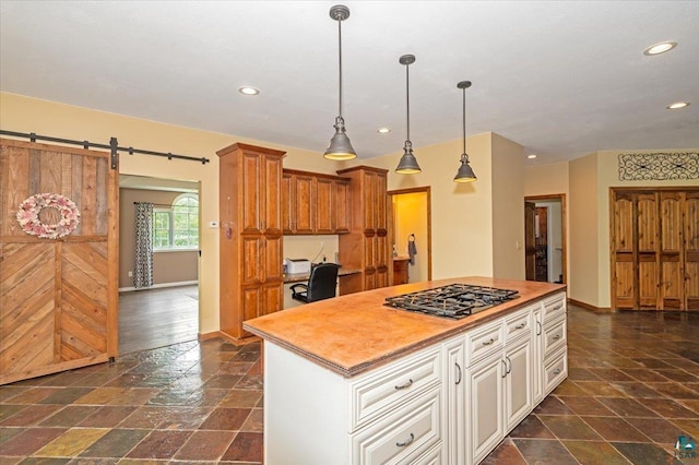 kitchen featuring stainless steel gas stovetop, a kitchen island, a barn door, dark tile patterned flooring, and pendant lighting