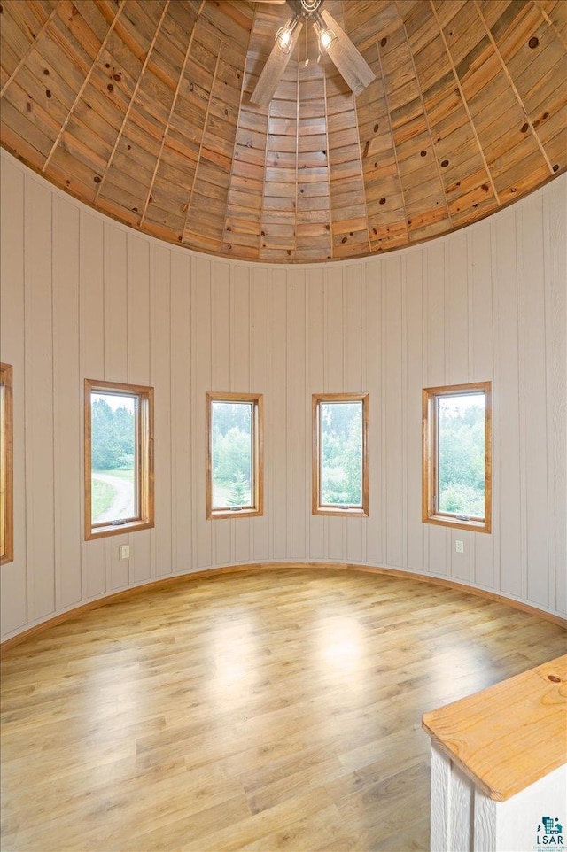 spare room featuring ceiling fan, a high ceiling, wooden walls, light wood-type flooring, and wood ceiling