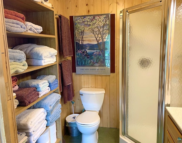 bathroom featuring an enclosed shower, wood walls, vanity, and toilet