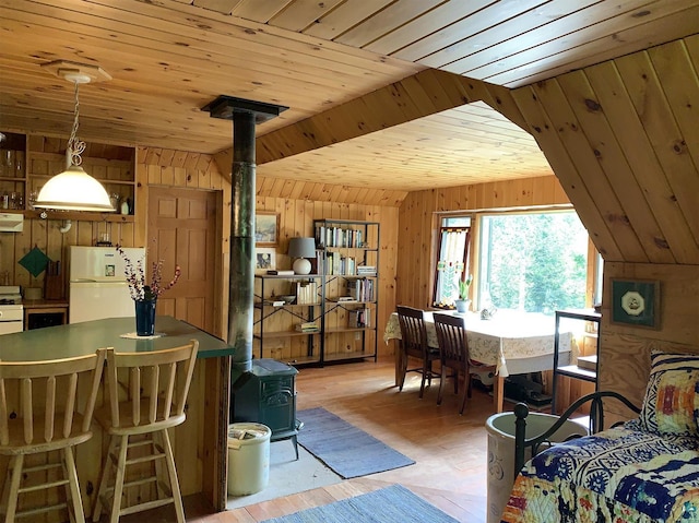 interior space with hanging light fixtures, wood walls, white appliances, and a wood stove