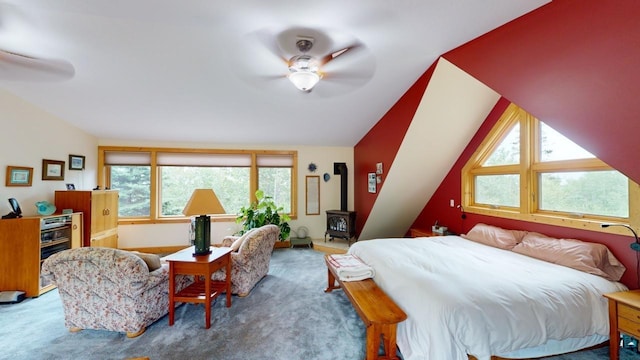 bedroom featuring vaulted ceiling, carpet flooring, a wood stove, and ceiling fan