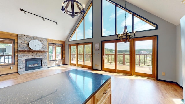 unfurnished living room with a stone fireplace, light wood finished floors, a healthy amount of sunlight, and an inviting chandelier