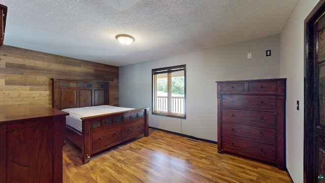 bedroom with a textured ceiling, wooden walls, and light wood-style floors