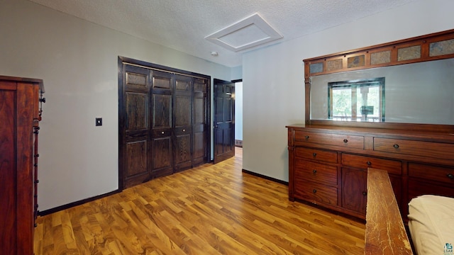 bedroom featuring baseboards, attic access, light wood-style floors, and a textured ceiling