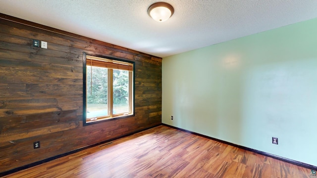 spare room with a textured ceiling, wooden walls, wood finished floors, and baseboards