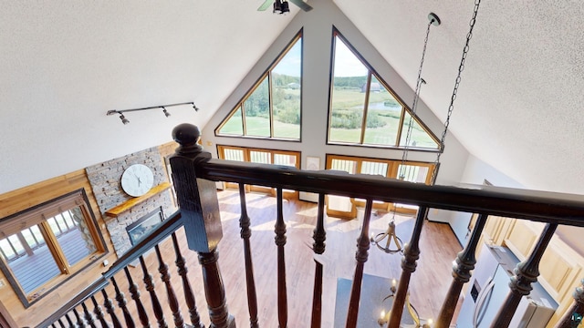 staircase featuring rail lighting, high vaulted ceiling, a textured ceiling, and wood finished floors