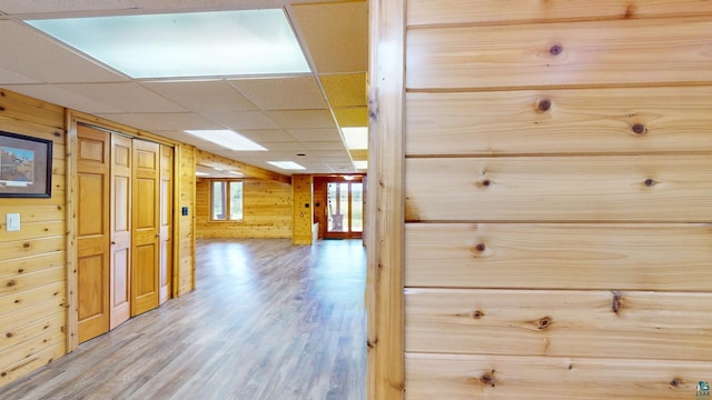 hallway with wooden walls, wood finished floors, and a paneled ceiling