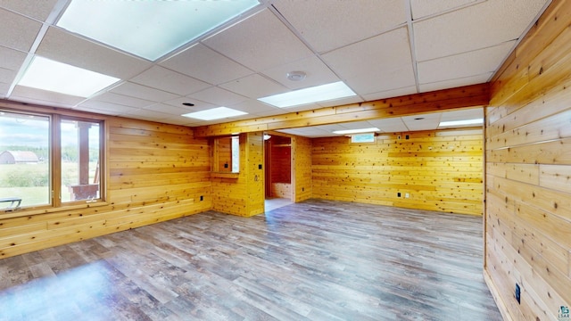 empty room with a paneled ceiling, wood finished floors, and wood walls