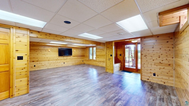 empty room featuring wood walls, a drop ceiling, and wood finished floors