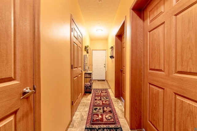 hallway with a textured ceiling and light tile patterned flooring