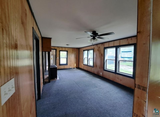 spare room with a ceiling fan, dark carpet, and wood walls