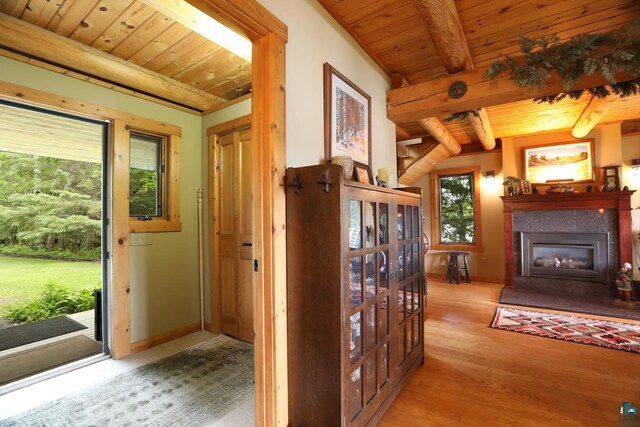 interior space featuring light wood-type flooring, a tiled fireplace, wooden ceiling, and beam ceiling