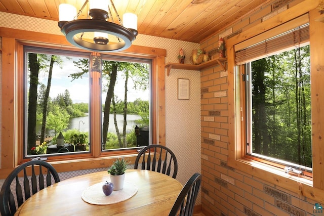 dining space with a water view, brick wall, a notable chandelier, and wooden ceiling