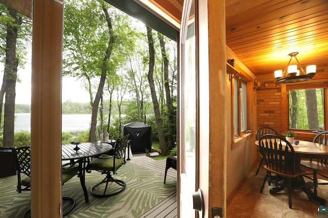 sunroom / solarium with a water view, wood ceiling, and a notable chandelier