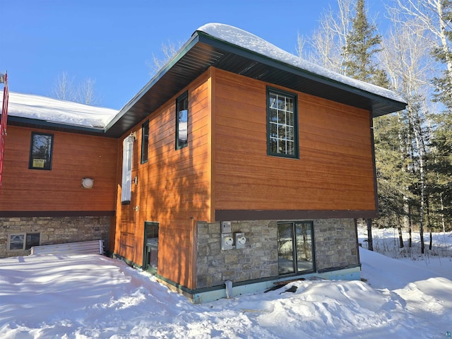 view of snow covered exterior with stone siding