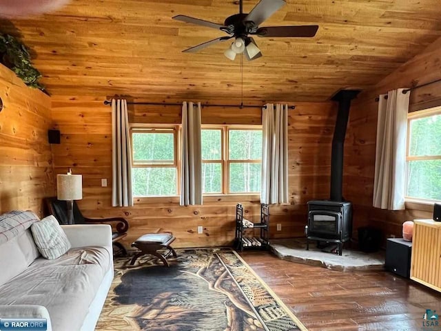 living area featuring ceiling fan, wooden walls, wood ceiling, wood-type flooring, and a wood stove