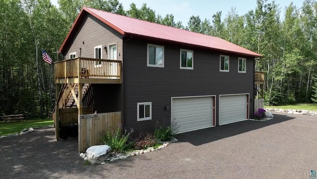 view of property exterior featuring metal roof, aphalt driveway, an attached garage, stairs, and a deck