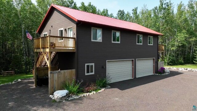 view of side of property featuring metal roof, an attached garage, driveway, stairway, and a wooden deck