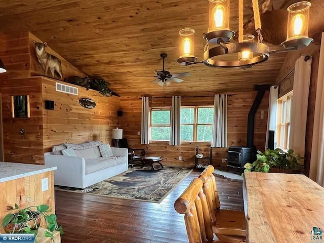 living area with vaulted ceiling, a wood stove, wood ceiling, and wooden walls