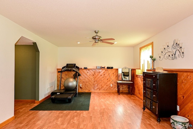 exercise room with light wood-type flooring, wood walls, ceiling fan, and a textured ceiling