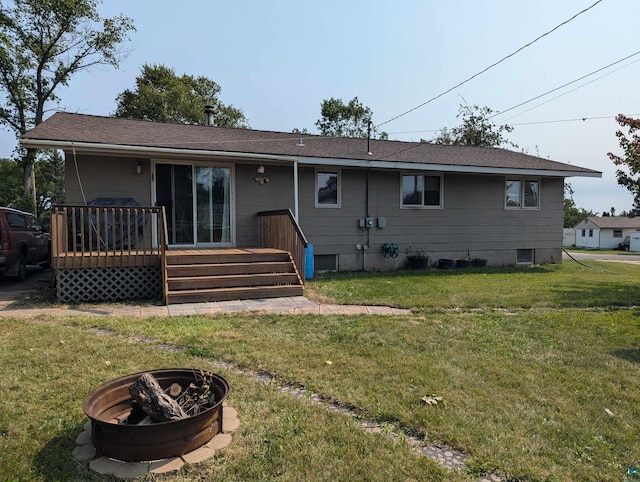 rear view of house with a wooden deck, a lawn, and an outdoor fire pit