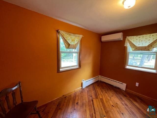 unfurnished room with a baseboard heating unit, wood-type flooring, and a wall mounted air conditioner