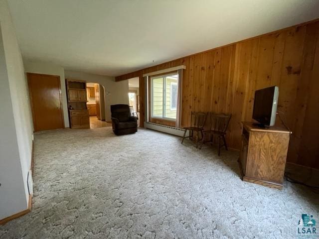 unfurnished living room featuring a baseboard heating unit, carpet, and wood walls