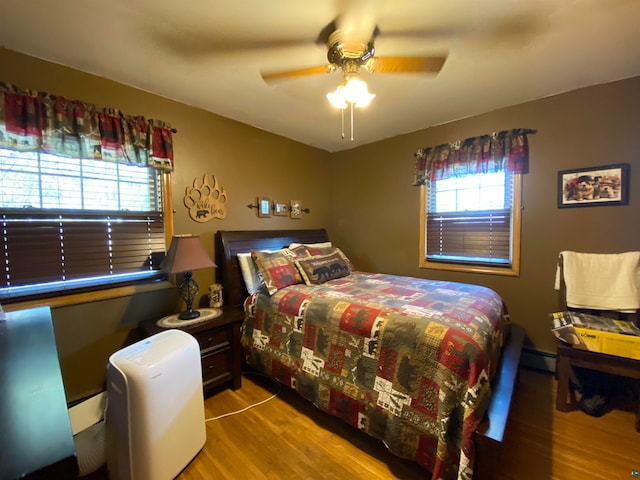 bedroom with ceiling fan, light wood-type flooring, and a baseboard heating unit