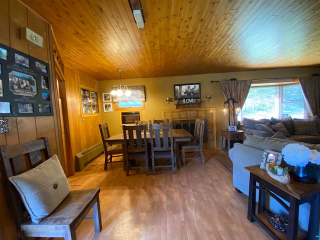 dining room featuring wood walls, wooden ceiling, wood-type flooring, an inviting chandelier, and a baseboard radiator