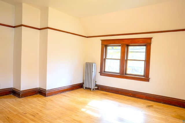 spare room featuring lofted ceiling, hardwood / wood-style floors, and radiator