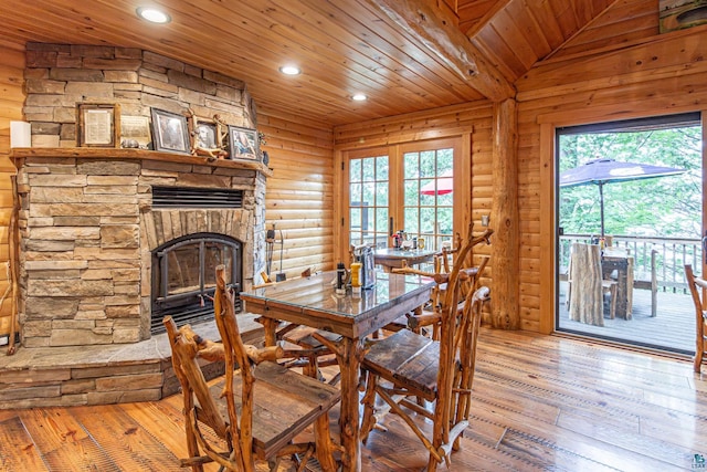 dining area featuring light hardwood / wood-style floors, vaulted ceiling, a stone fireplace, wooden ceiling, and french doors