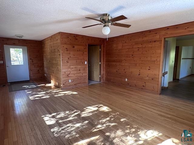 empty room featuring ceiling fan, a textured ceiling, wood walls, and dark wood-type flooring