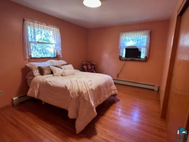 bedroom featuring multiple windows, baseboard heating, and hardwood / wood-style flooring