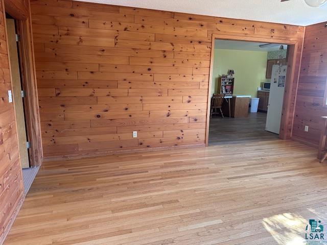 unfurnished room featuring ceiling fan, light hardwood / wood-style flooring, and wood walls