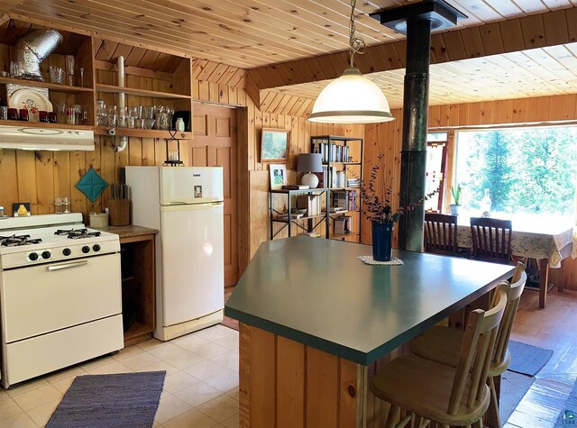 kitchen featuring wood walls, wood ceiling, vaulted ceiling, pendant lighting, and white appliances