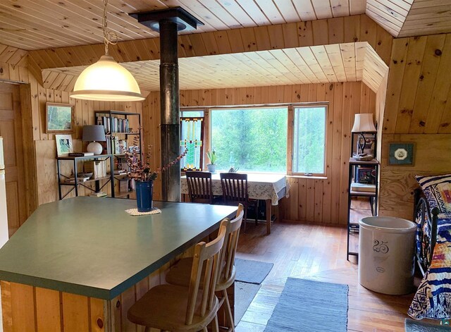 dining area with lofted ceiling, wood ceiling, light hardwood / wood-style flooring, a wood stove, and wooden walls