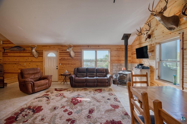 living room featuring lofted ceiling, wood walls, light tile patterned floors, and a wood stove